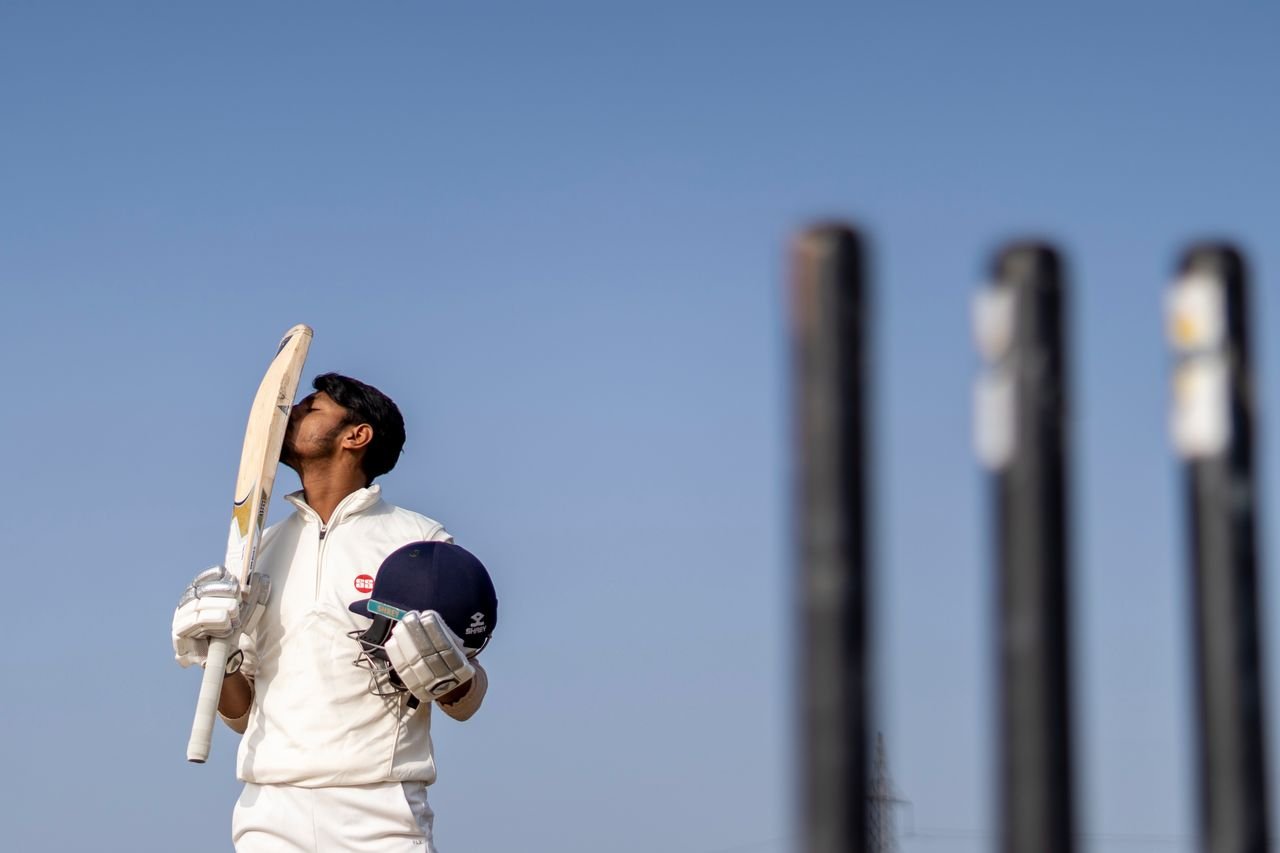 About Cricket player in uniform celebrating a game-winning shot by kissing his bat on a sunny day.