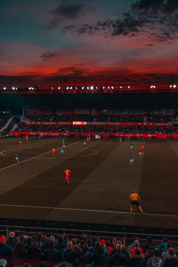 Menu Wide-angle view of a soccer match taking place in a stadium at sunset with a vibrant sky.