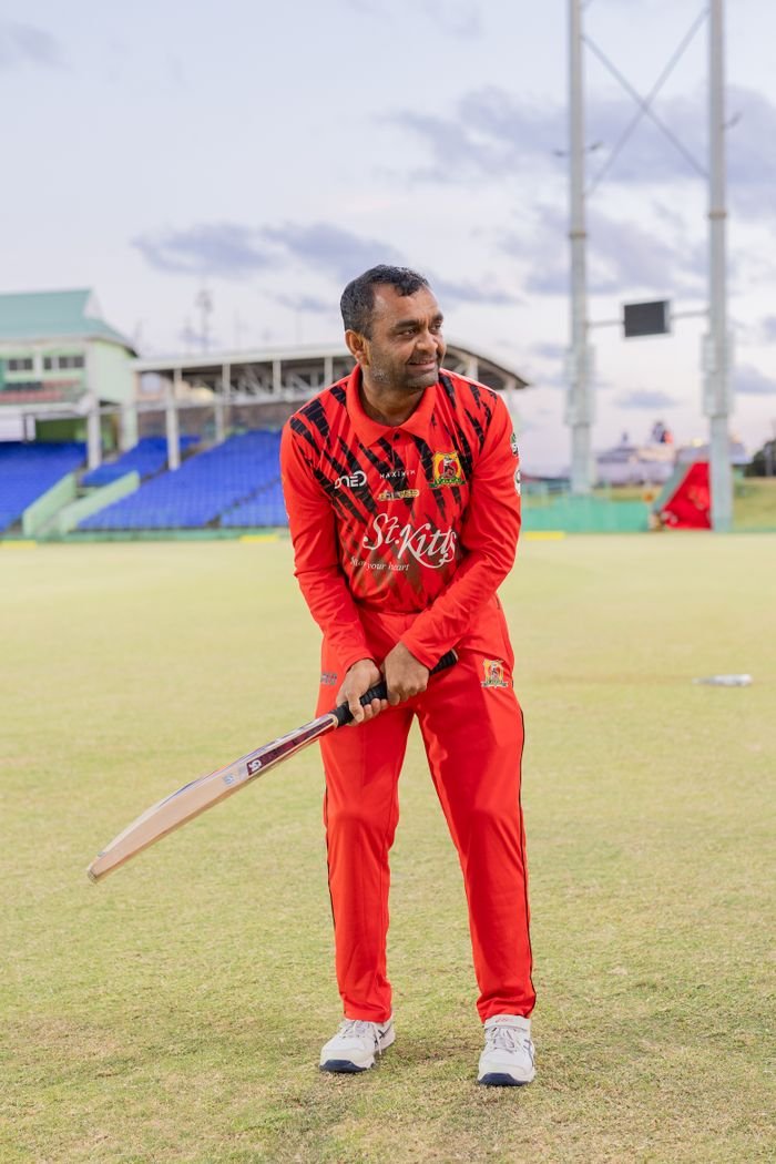 Menu Cricketer in red uniform practicing on a Saint Kitts sports field during the day.