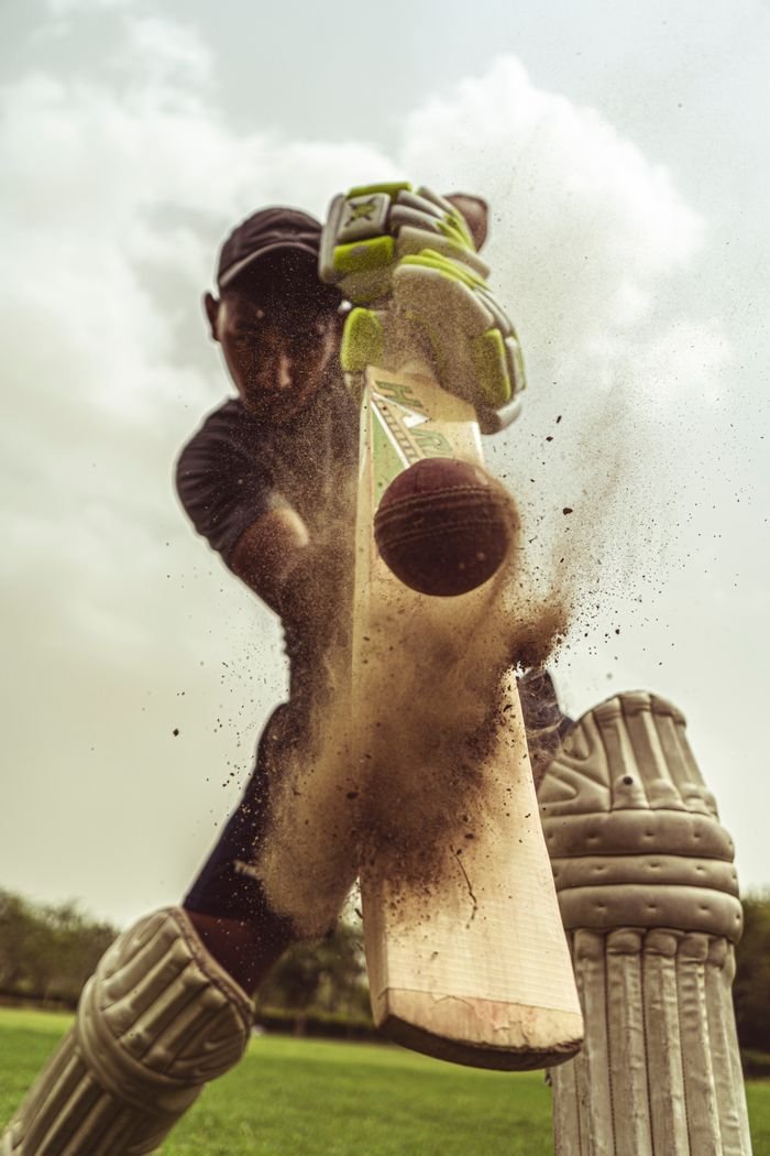 Menu Cricketer in motion striking the ball with intense focus, clouds of dust captured.