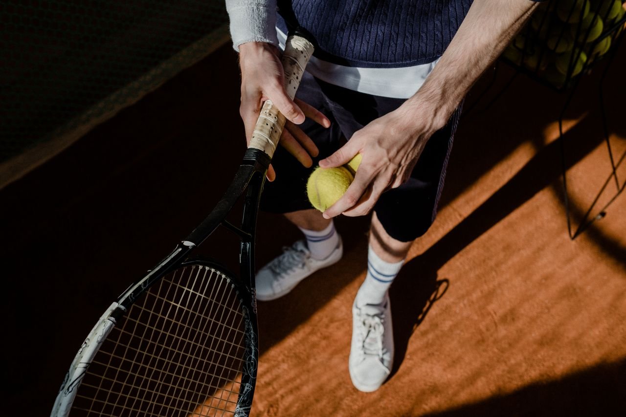 Menu A tennis player prepares for a serve, holding a racket and tennis ball on a clay court.